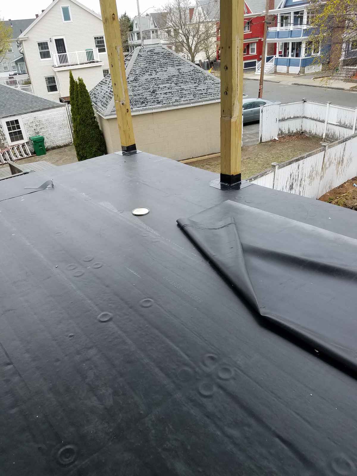 Black rubber roofing membrane laid on a flat roof with a seam detail, houses behind