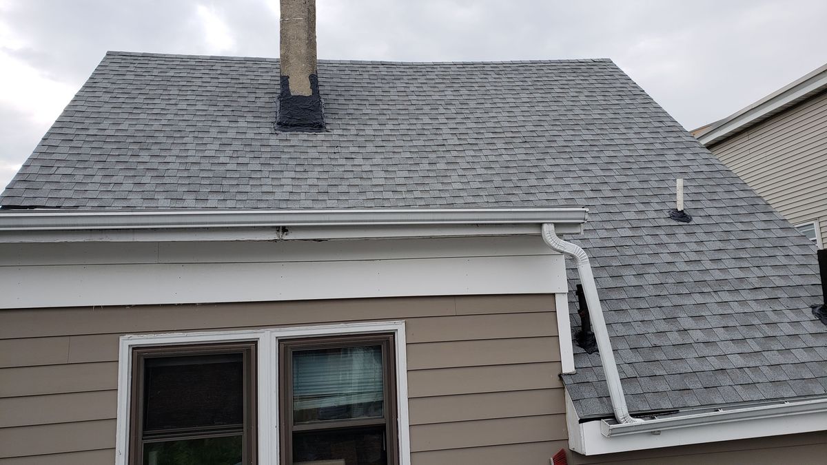 Gray asphalt shingle roof with chimney and new white gutter on a beige house after installation